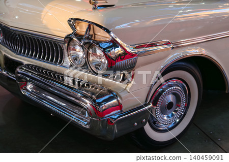 Closeup photo of a white vintage luxury automobile with chrome headlights, retro grille, and whitewall tires. Historic classic car displayed in a museum with polished metal reflections and elegant Closeup photo of a white vintage luxury automobile with chrome headlights, retro grille, and whitewall tires. Historic classic car displayed in a museum with polished metal reflections and elegant 140459091