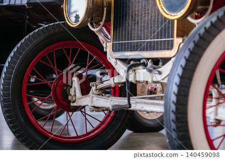 Vintage antique automobile with red spoked wheels and historic mechanical suspension details displayed inside a retro car museum. Classic transportation vehicle showcases early automotive Vintage antique automobile with red spoked wheels and historic mechanical suspension details displayed inside a retro car museum. Classic transportation vehicle showcases early automotive 140459098