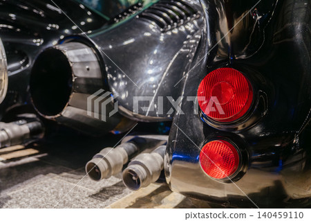 Close-up view captures rear of custom-designed black vehicle. Reflective body showcases two circular red taillights and a large exhaust nozzle, emphasizing unique design and mechanical features. 140459110