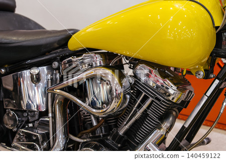 Detailed close-up showcases custom motorcycle engine and vibrant yellow fuel tank. Intricate chrome components highlight craftsmanship, with a textured black leather seat partially visible. Detailed close-up showcases custom motorcycle engine and vibrant yellow fuel tank. Intricate chrome components highlight craftsmanship, with a textured black leather seat partially visible. 140459122
