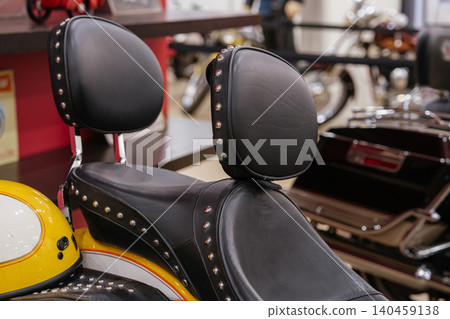 Close-up shot highlights custom motorcycle seat and backrest, upholstered in black leather with polished metal studs. A yellow and white motorcycle helmet is partially visible, suggesting rider Close-up shot highlights custom motorcycle seat and backrest, upholstered in black leather with polished metal studs. A yellow and white motorcycle helmet is partially visible, suggesting rider 140459138