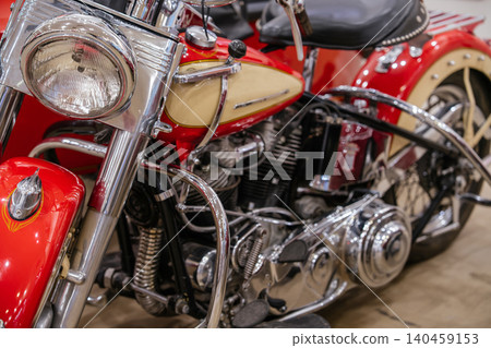 Close-up shot captures vintage red and cream motorcycle showcasing gleaming chrome handlebars, headlight, and engine. Intricate details highlight the classic design and well-maintained condition. 140459153