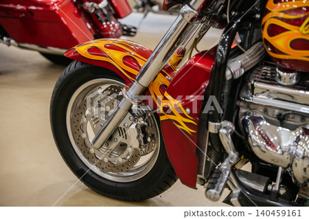Detailed close-up captures custom motorcycle's front wheel and fender, showcasing vibrant flame graphics in yellow and orange against deep red paint. Polished chrome suspension and brake disc enhance 140459161