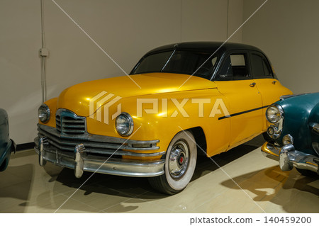 Vintage yellow and black sedan showcases classic automotive design in pristine condition. Gleaming metallic body and chrome detailing reflect the indoor lighting, enhancing its appeal. Vintage yellow and black sedan showcases classic automotive design in pristine condition. Gleaming metallic body and chrome detailing reflect the indoor lighting, enhancing its appeal. 140459200