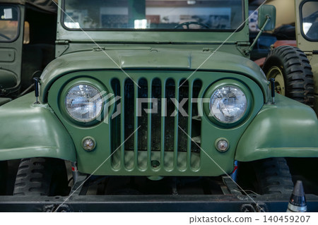 Detailed frontal view of vintage olive-drab military utility vehicle. Iconic seven-slot grille and round headlights highlight rugged design, suggesting historical significance in outdoor setting. Detailed frontal view of vintage olive-drab military utility vehicle. Iconic seven-slot grille and round headlights highlight rugged design, suggesting historical significance in outdoor setting. 140459207