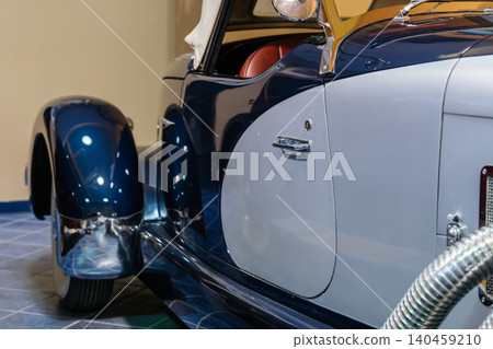 Close-up view highlights vintage two-tone convertible car featuring navy blue and light grey colors. Chrome accents and tan leather interior visible through open window, showcasing classic design Close-up view highlights vintage two-tone convertible car featuring navy blue and light grey colors. Chrome accents and tan leather interior visible through open window, showcasing classic design 140459210