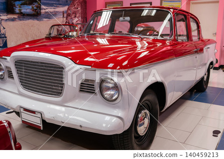 Close-up view of a classic two-tone red and white sedan showcased in a museum. Pristine condition highlights vintage appeal, with reflections on polished chrome and tiled flooring enhancing the Close-up view of a classic two-tone red and white sedan showcased in a museum. Pristine condition highlights vintage appeal, with reflections on polished chrome and tiled flooring enhancing the 140459213