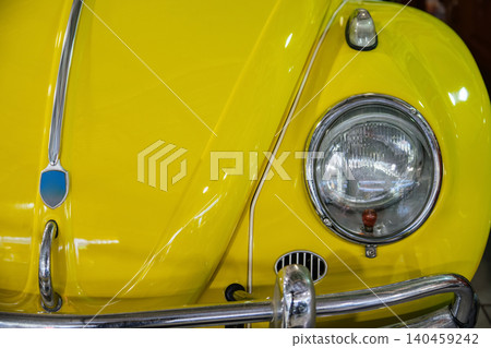 Close-up view captures front detail of vintage yellow car, showcasing glossy paint and chrome accents. Key features include headlight, bumper, and distinctive emblem, highlighting retro design. Close-up view captures front detail of vintage yellow car, showcasing glossy paint and chrome accents. Key features include headlight, bumper, and distinctive emblem, highlighting retro design. 140459242