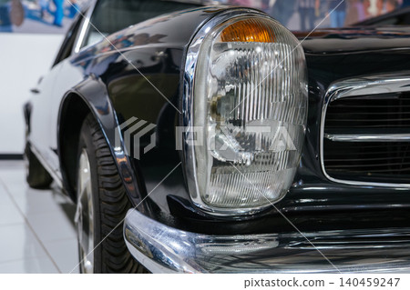 Detailed close-up captures front end of vintage two-tone automobile in black and white. Chrome grille and amber turn signal highlight classic design, reflecting surroundings in bright showroom Detailed close-up captures front end of vintage two-tone automobile in black and white. Chrome grille and amber turn signal highlight classic design, reflecting surroundings in bright showroom 140459247
