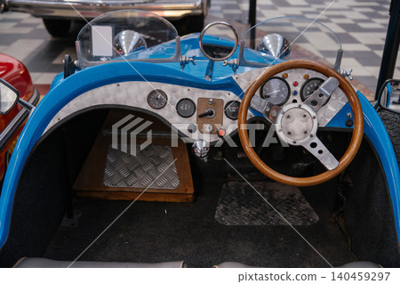 Close-up view of vintage-style blue open-top car interior, showcasing dashboard details. Features classic wooden steering wheel, chrome gear shift, and multiple analog gauges against brushed metal and Close-up view of vintage-style blue open-top car interior, showcasing dashboard details. Features classic wooden steering wheel, chrome gear shift, and multiple analog gauges against brushed metal and 140459297