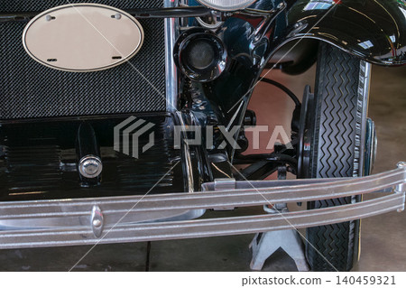 Classic antique car showcases intricate hood ornament and vintage grille in well-lit garage. Nostalgic atmosphere highlights craftsmanship and timeless design. 140459321
