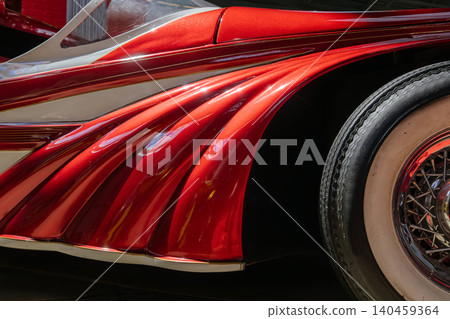 Detailed close-up view highlights the vibrant metallic red rear fender of a classic custom car. Elegant fluted design and chrome accents reflect light, showcasing automotive craftsmanship. Detailed close-up view highlights the vibrant metallic red rear fender of a classic custom car. Elegant fluted design and chrome accents reflect light, showcasing automotive craftsmanship. 140459364