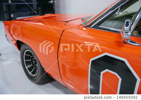 Detailed low-angle view of classic orange car side. Image highlights glossy finish, sharp body lines, and features like fender, door panel, multi-spoke wheel, and chrome side mirror. Detailed low-angle view of classic orange car side. Image highlights glossy finish, sharp body lines, and features like fender, door panel, multi-spoke wheel, and chrome side mirror. 140459392