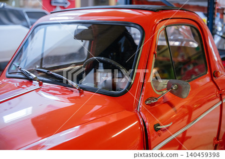 Close-up shot captures vibrant red vintage car showcasing polished exterior features. Highlights include windshield, wipers, side mirror, door handle, and sunroof, suggesting an indoor showroom Close-up shot captures vibrant red vintage car showcasing polished exterior features. Highlights include windshield, wipers, side mirror, door handle, and sunroof, suggesting an indoor showroom 140459398