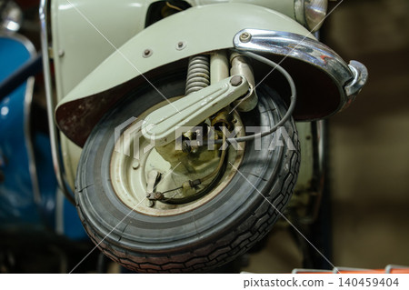Detailed low-angle view captures front wheel, suspension system, and fender of vintage scooter. Light green body features polished chrome accents, showcasing retro design and mechanical elements. Detailed low-angle view captures front wheel, suspension system, and fender of vintage scooter. Light green body features polished chrome accents, showcasing retro design and mechanical elements. 140459404