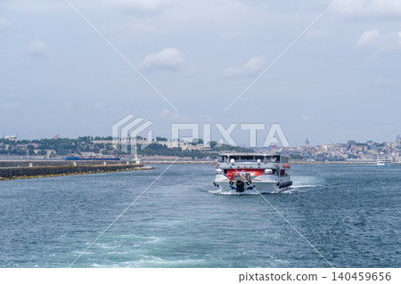 A tour boat navigates the waters of the Bosphorus strait, with a stunning skyline featuring historic buildings and a vibrant atmosphere on a sunny day. A tour boat navigates the waters of the Bosphorus strait, with a stunning skyline featuring historic buildings and a vibrant atmosphere on a sunny day. 140459656