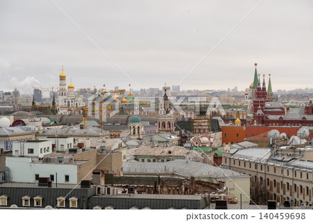 Overview of Moscows skyline showing iconic structures such as cathedrals and the Kremlin, highlighted by a gray sky and urban rooftops below. 140459698