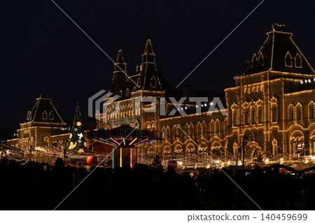 Colorful lights adorn a magnificent historic structure while visitors enjoy festive activities and holiday decorations in a vibrant market atmosphere. Colorful lights adorn a magnificent historic structure while visitors enjoy festive activities and holiday decorations in a vibrant market atmosphere. 140459699
