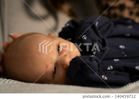 A precious baby lies comfortably on a soft blanket, looking around with wide eyes and a gentle expression, exuding innocence and tranquility indoors. A precious baby lies comfortably on a soft blanket, looking around with wide eyes and a gentle expression, exuding innocence and tranquility indoors. 140459712