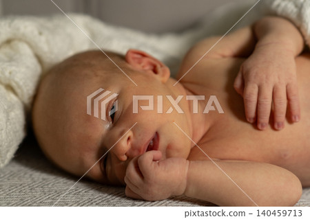 A newborn baby lies on a soft blanket, displaying a serene expression while gently holding a finger in their mouth, radiating innocence and tranquility. A newborn baby lies on a soft blanket, displaying a serene expression while gently holding a finger in their mouth, radiating innocence and tranquility. 140459713