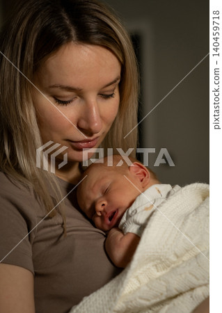 Mother cradles her newborn closely, creating a peaceful bond while enjoying a quiet moment in a softly lit room during the evening. Mother cradles her newborn closely, creating a peaceful bond while enjoying a quiet moment in a softly lit room during the evening. 140459718