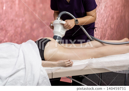 Client relaxes on a treatment table while a therapist performs body contouring with specialized equipment in a serene wellness spa environment. Client relaxes on a treatment table while a therapist performs body contouring with specialized equipment in a serene wellness spa environment. 140459731
