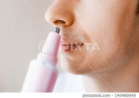 Close-up of a man using an electric trimmer for nose hair removal. A daily male grooming routine and personal facial care for health and hygiene. Close-up of a man using an electric trimmer for nose hair removal. A daily male grooming routine and personal facial care for health and hygiene. 140460049