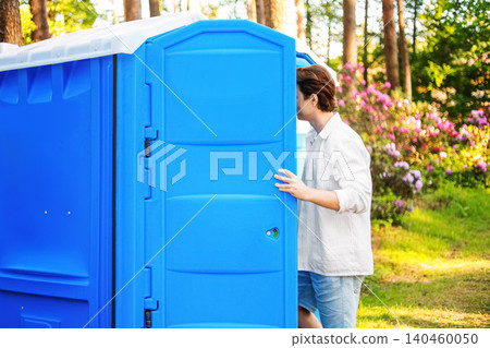 Man entering a blue outdoor portable toilet. Experiencing an urgent toilet emergency due to an upset stomach, diarrhea, and digestive discomfort from food poisoning. Man entering a blue outdoor portable toilet. Experiencing an urgent toilet emergency due to an upset stomach, diarrhea, and digestive discomfort from food poisoning. 140460050