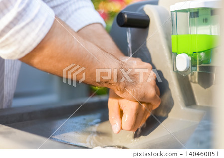 Man washing hands with soap and water at an outdoor portable sink. Essential personal hygiene procedure for disease and infection prevention at a campground or campsite. Man washing hands with soap and water at an outdoor portable sink. Essential personal hygiene procedure for disease and infection prevention at a campground or campsite. 140460051