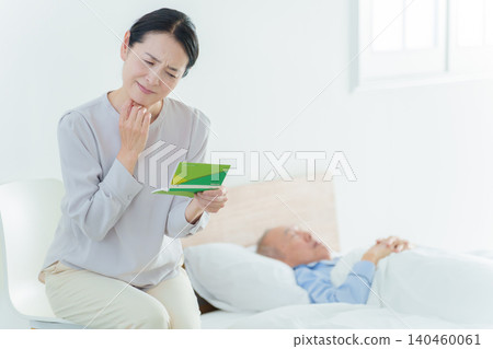 A woman with a troubled expression looks at her bankbook; she has gone bankrupt due to caregiving responsibilities. A woman with a troubled expression looks at her bankbook; she has gone bankrupt due to caregiving responsibilities. 140460061