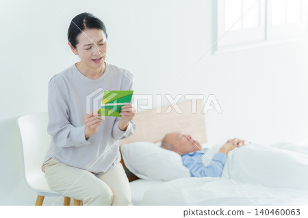 A woman with a troubled expression looks at her bankbook; she has gone bankrupt due to caregiving responsibilities. A woman with a troubled expression looks at her bankbook; she has gone bankrupt due to caregiving responsibilities. 140460063