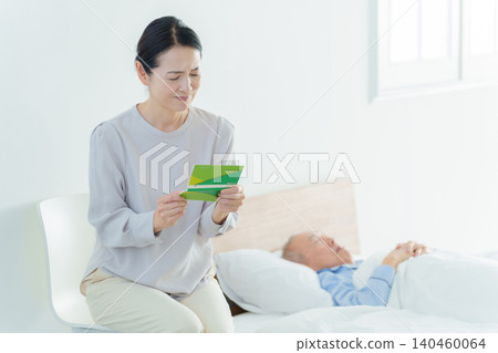一位神情憂慮的女士看著她的銀行存摺;由於承擔了照顧家人的責任,她已經破產了。 一位神情憂慮的女士看著她的銀行存摺;由於承擔了照顧家人的責任,她已經破產了。 140460064
