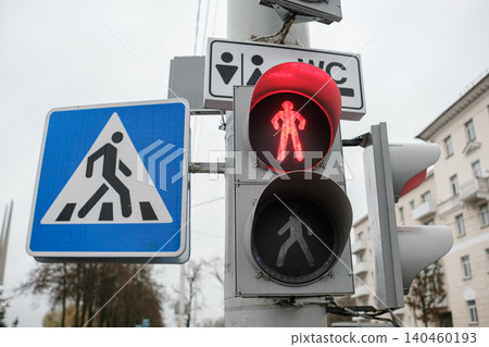 A red walk signal is displayed at a crosswalk along with a caution sign. 140460193