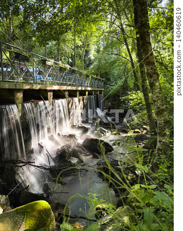 Serene waterfall flows beneath a scenic wooden walkway at Passadicos do Rio Uima in Pigeiros Portugal surrounded by lush tranquil forest greenery 140460619