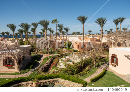 Expansive garden featuring lush greenery and palm trees, set against a tranquil coastal backdrop under a clear blue sky during daytime. Expansive garden featuring lush greenery and palm trees, set against a tranquil coastal backdrop under a clear blue sky during daytime. 140460949