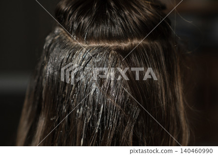 A client receives hair coloring treatment in a salon, showcasing the application of dye on the roots and mid-lengths of their hair. 140460990