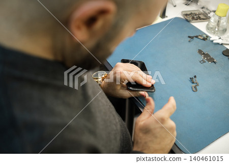 A person is working on repairing a smartphone on a blue work mat in a busy workshop, surrounded by various tools and small parts. A person is working on repairing a smartphone on a blue work mat in a busy workshop, surrounded by various tools and small parts. 140461015