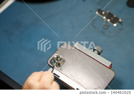 A person is fixing a smartphone camera lens on a work surface with tools and parts nearby during the afternoon time of day. A person is fixing a smartphone camera lens on a work surface with tools and parts nearby during the afternoon time of day. 140461020
