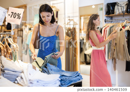 Two girls customer chooses jeans in store, and buyer carefully examines product. Two girls customer chooses jeans in store, and buyer carefully examines product. 140461509
