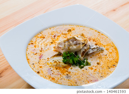Tasty creamy soup with white fish cod and greens at white plate 140461593