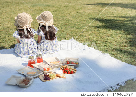 A photo of two sisters enjoying a picnic in a park, showing their backs and their lunch set (copy space available). A photo of two sisters enjoying a picnic in a park, showing their backs and their lunch set (copy space available). 140461787