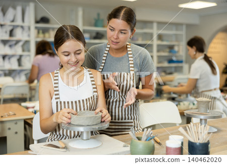 Female teacher explains to student how to make ceramics Female teacher explains to student how to make ceramics 140462020