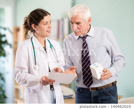 Girl doctor and senior male patient reviewing paper form, reading test results Girl doctor and senior male patient reviewing paper form, reading test results 140462028