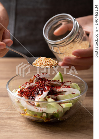 Woman hand pouring roasted sesame seed into a bowl with cucumber to making cucumber salad Woman hand pouring roasted sesame seed into a bowl with cucumber to making cucumber salad 140462134