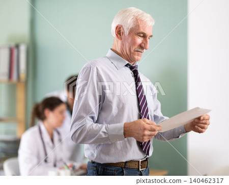 Elderly man holds prescriptions in his hands in the doctors office. Elderly man holds prescriptions in his hands in the doctors office. 140462317