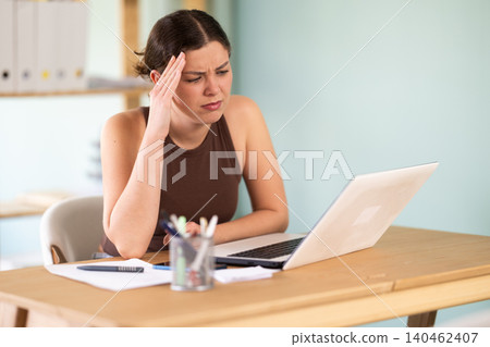 woman sitting at desk typing on laptop, she feels pms woman sitting at desk typing on laptop, she feels pms 140462407