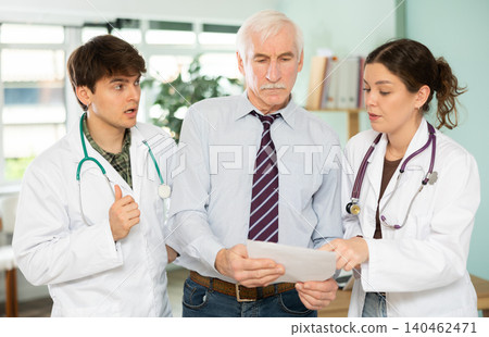 Two young doctors discuss with mature man patient medical test results Two young doctors discuss with mature man patient medical test results 140462471