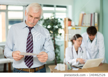 Elderly man holds prescriptions in his hands in the doctors office. Elderly man holds prescriptions in his hands in the doctors office. 140462526