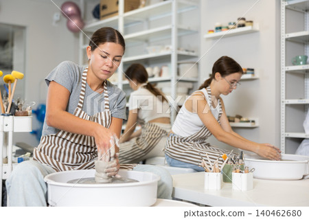 Three young women sits near potter wheel and makes clay crafts Three young women sits near potter wheel and makes clay crafts 140462680