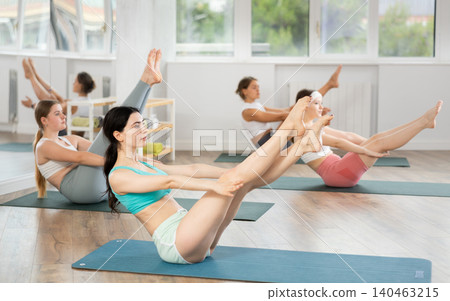 Girls practicing yoga performing Ardha Navasana, or half boat pose, balancing asana to strengthen abdominal muscles Girls practicing yoga performing Ardha Navasana, or half boat pose, balancing asana to strengthen abdominal muscles 140463215